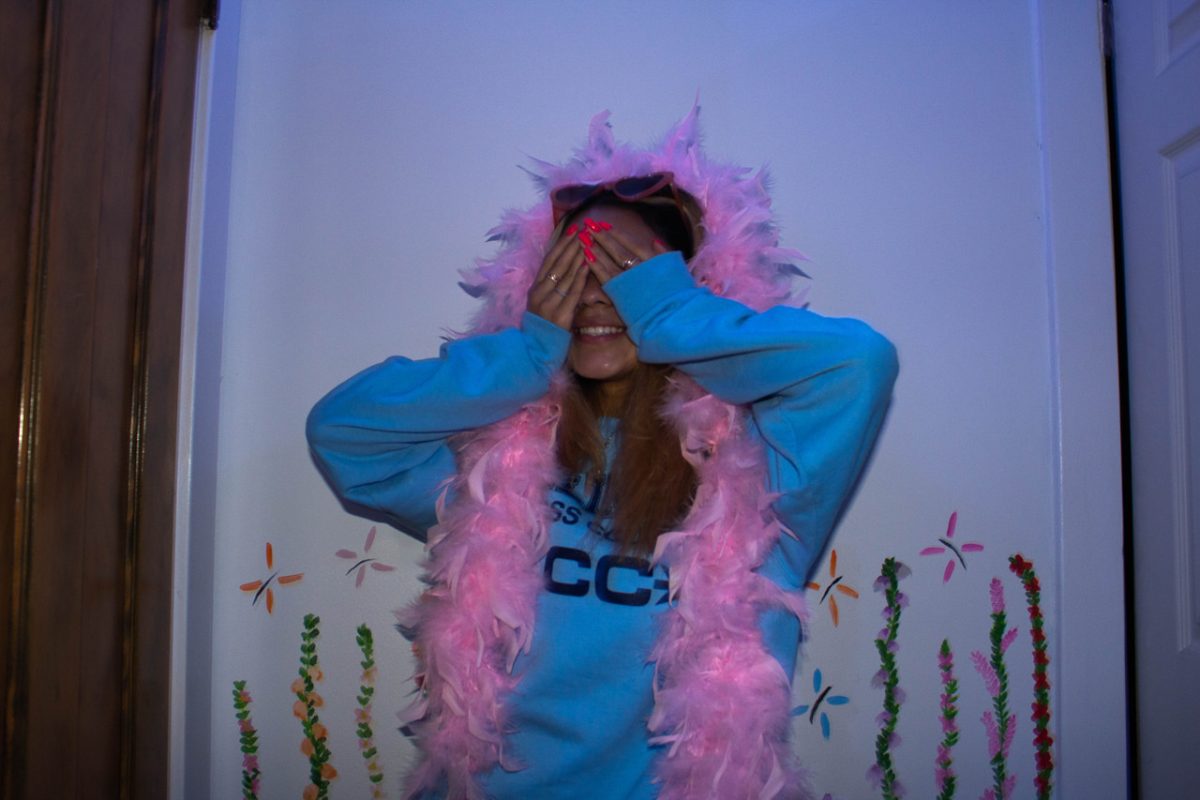 photo of a young woman smiling while wearing a pink scarf and her hands are covering her eyes