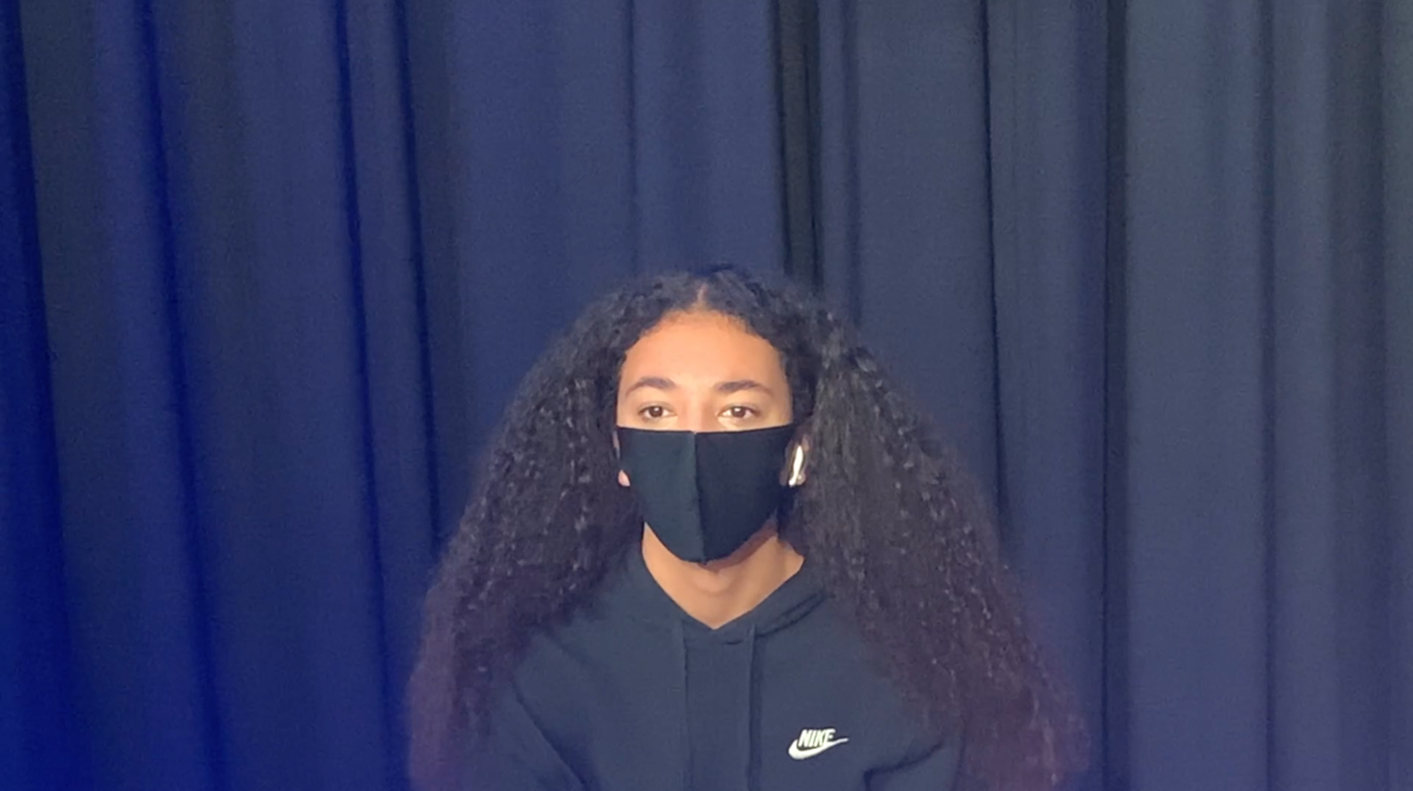Girl wearing a mask in front of a curtain in a nike sweater