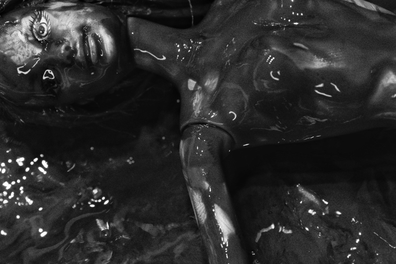 A photograph of a decaying barbie doll covered in black slime