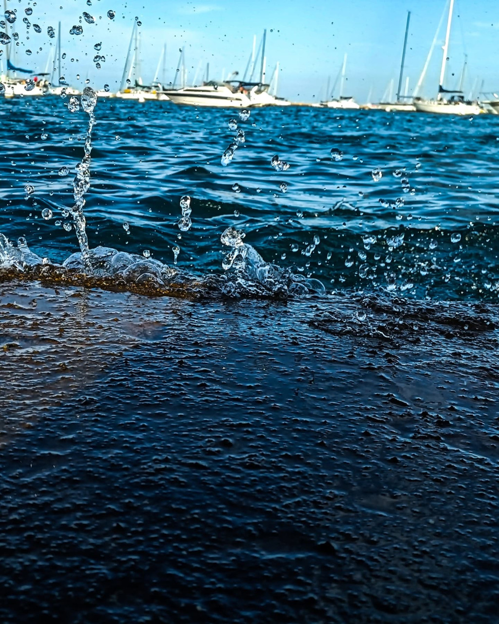 Photograph of wave crashing with boats in the background