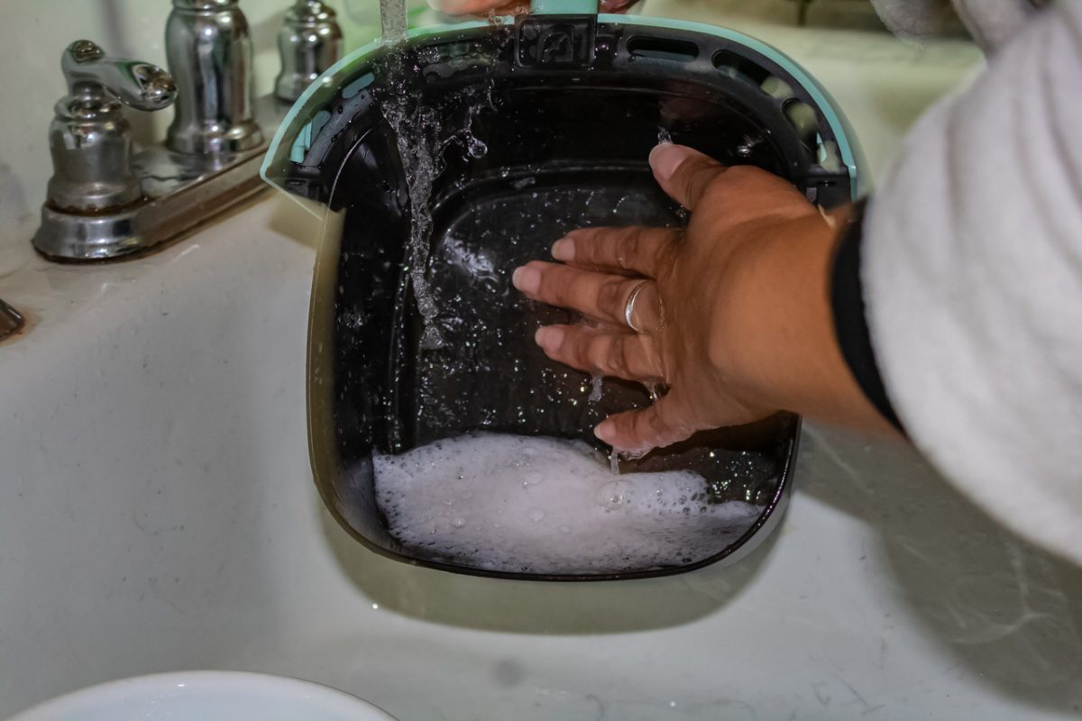 Photograph of a woman washing an air fryer with sud filled water