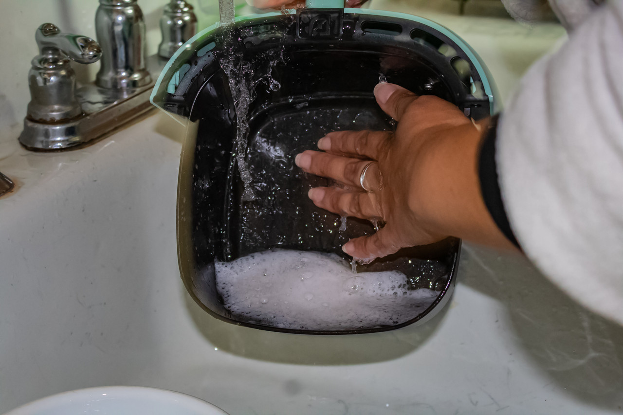 Photograph of a woman washing an air fryer with sud filled water