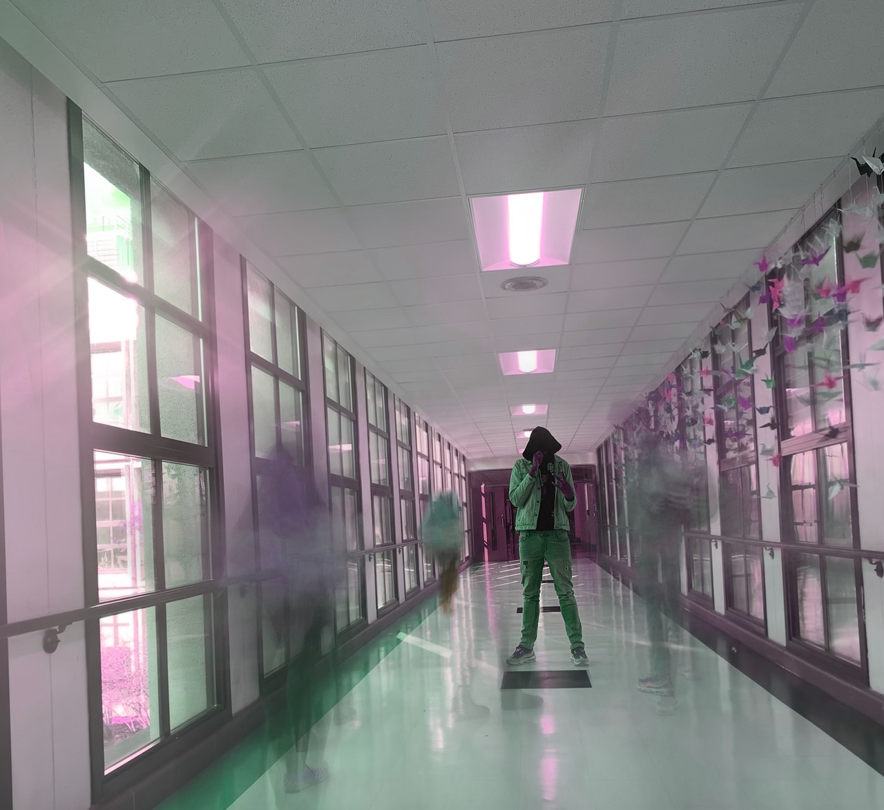 Still hooded figure in hallway with ghostly moving figures walking