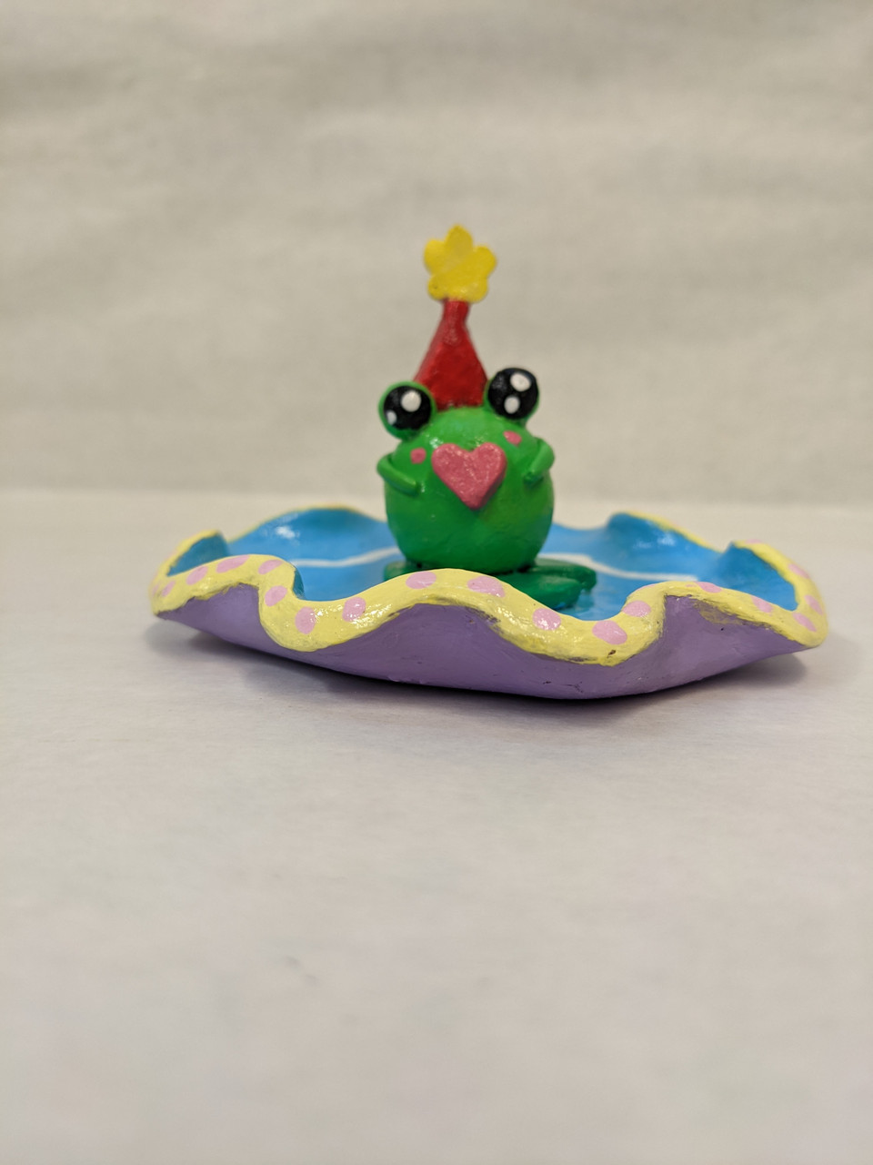 ceramic frog sitting on a purple plate with a red hat
