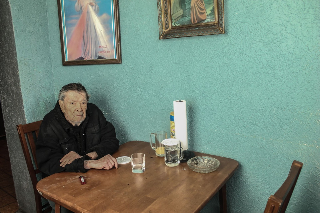 Photograph of a man sitting at a table in front of a green wall