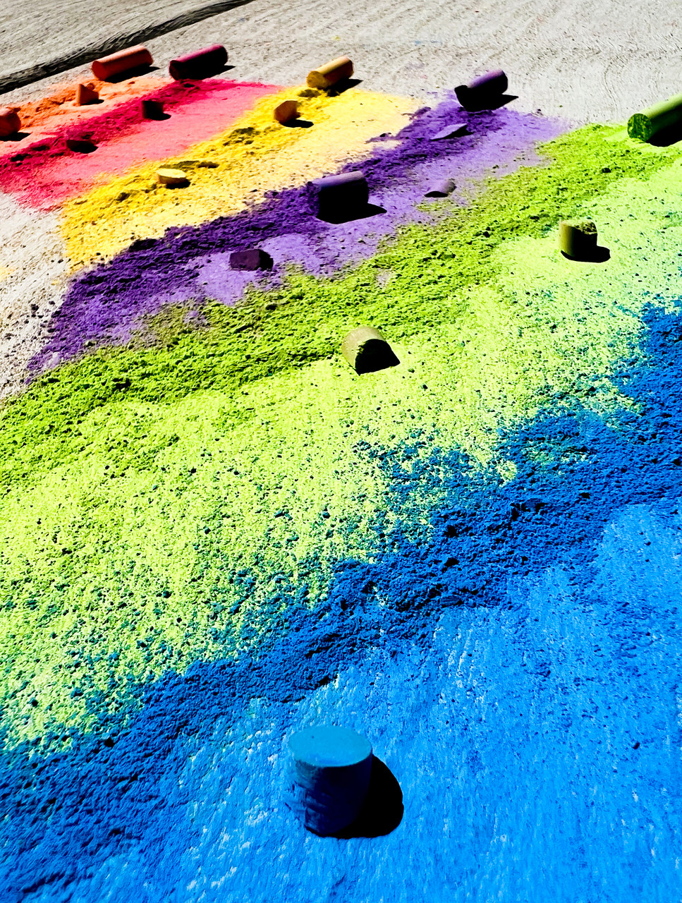 Photograph of a sidewalk colored with chalk with chalk pieces on top of differently colored rows.