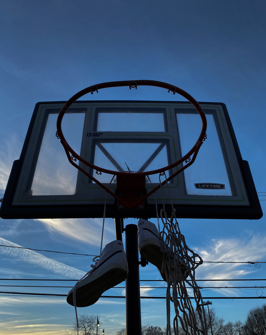 Photo of basketball hood from a lower perspective with shoes hanging off of the rim and a blue sky in the background.