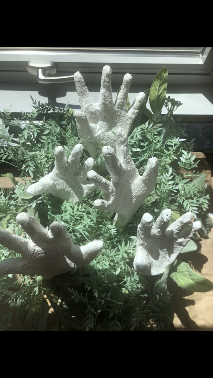 A sculpture of white hands surrounded by plants.