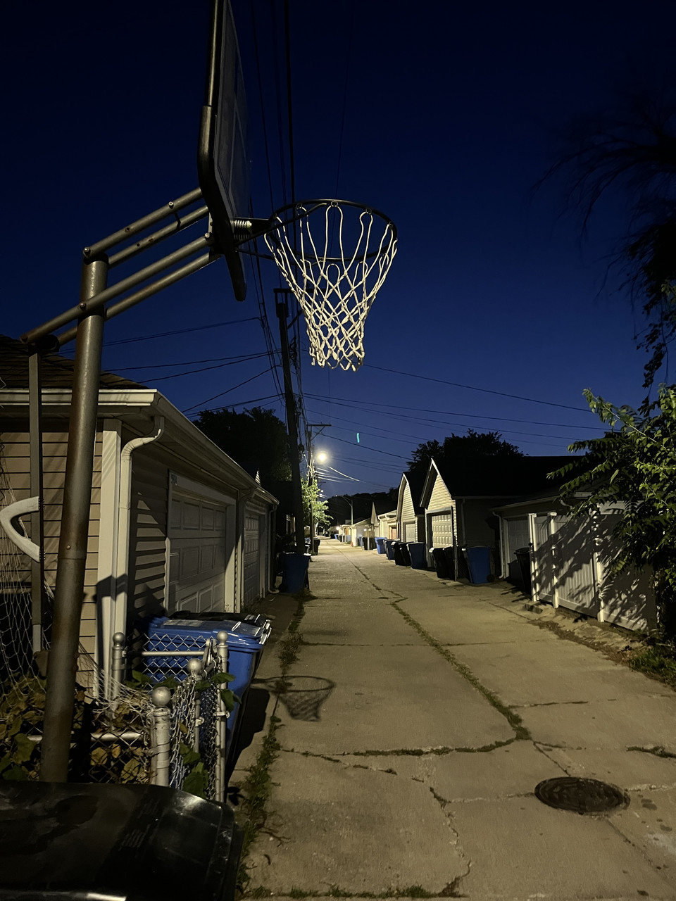 Photograph of an alley with a basketball hoop as the central aspect and houses in the background