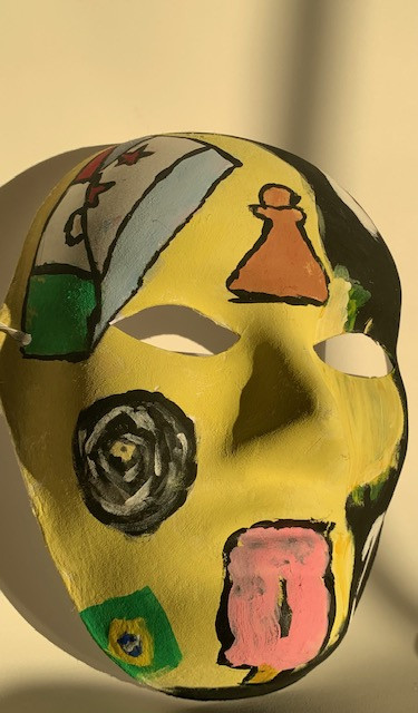Paper mache yellow and black mask with designs on it.