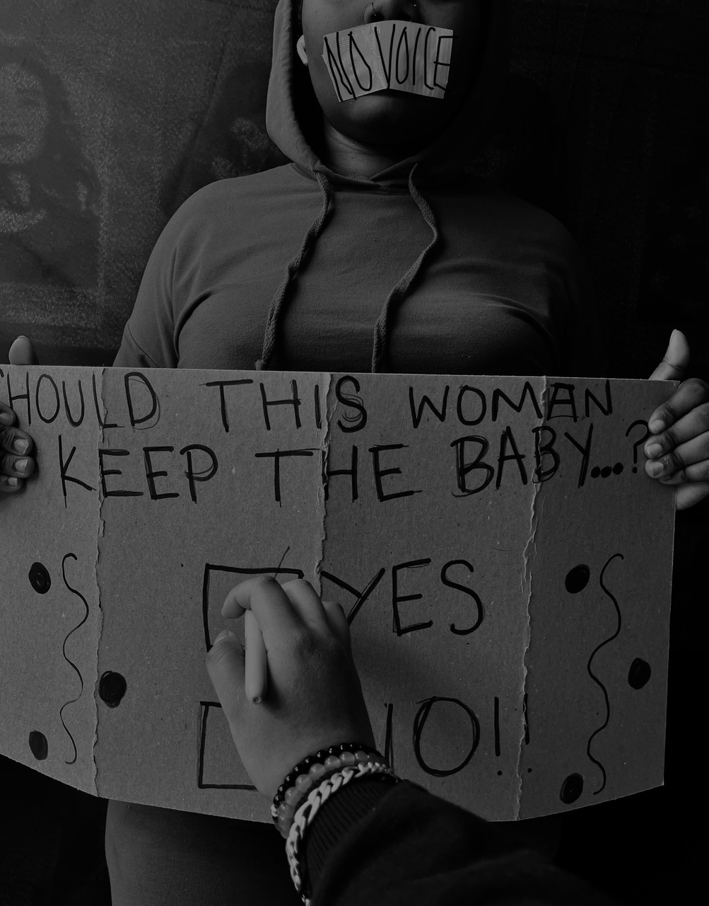 Black and white photo of person holding sign with tape over mouth.