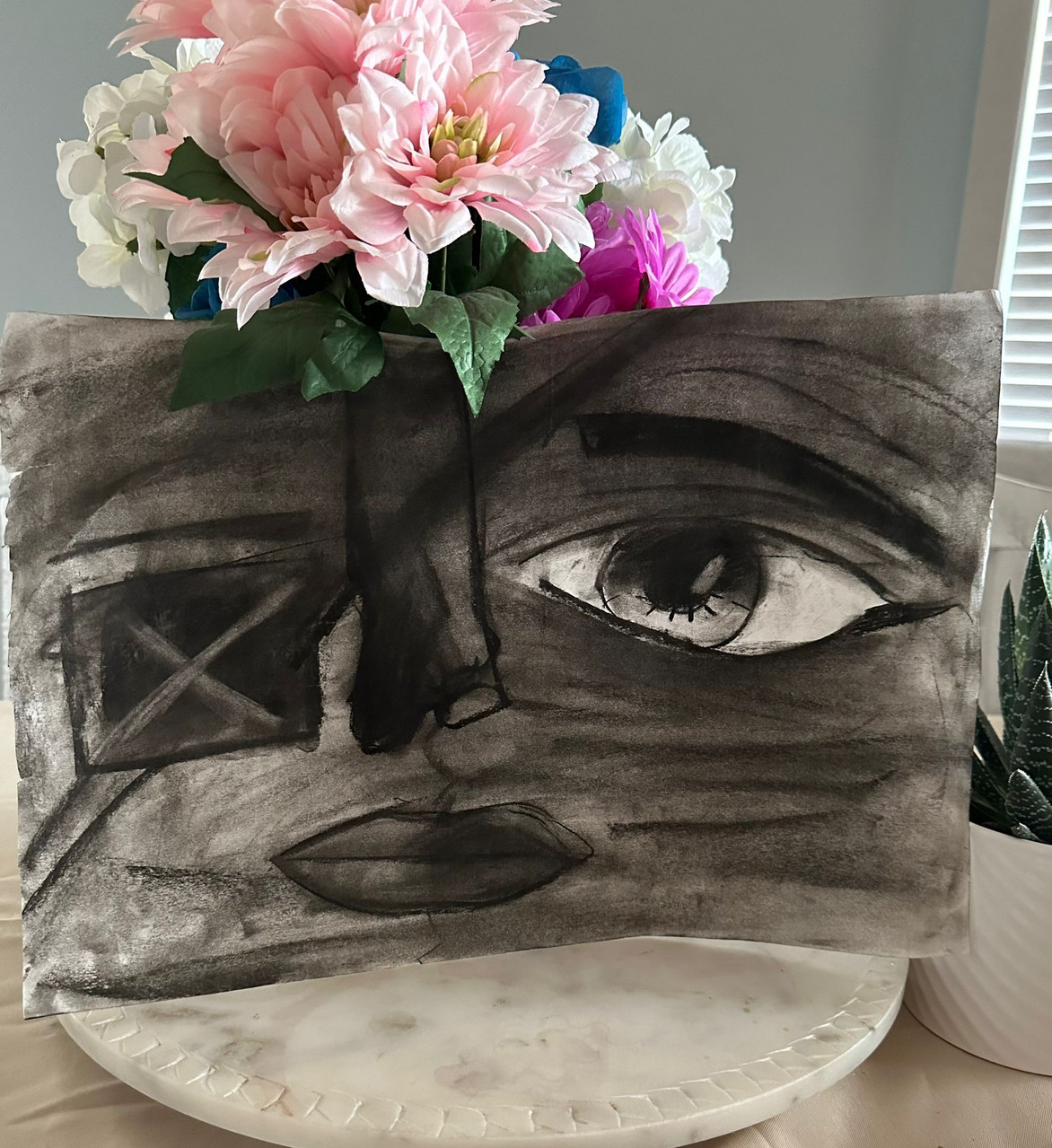 A drawing of a black and white face sits in front of a bouquet of flowers. There is an eye patch on the face in the drawing.