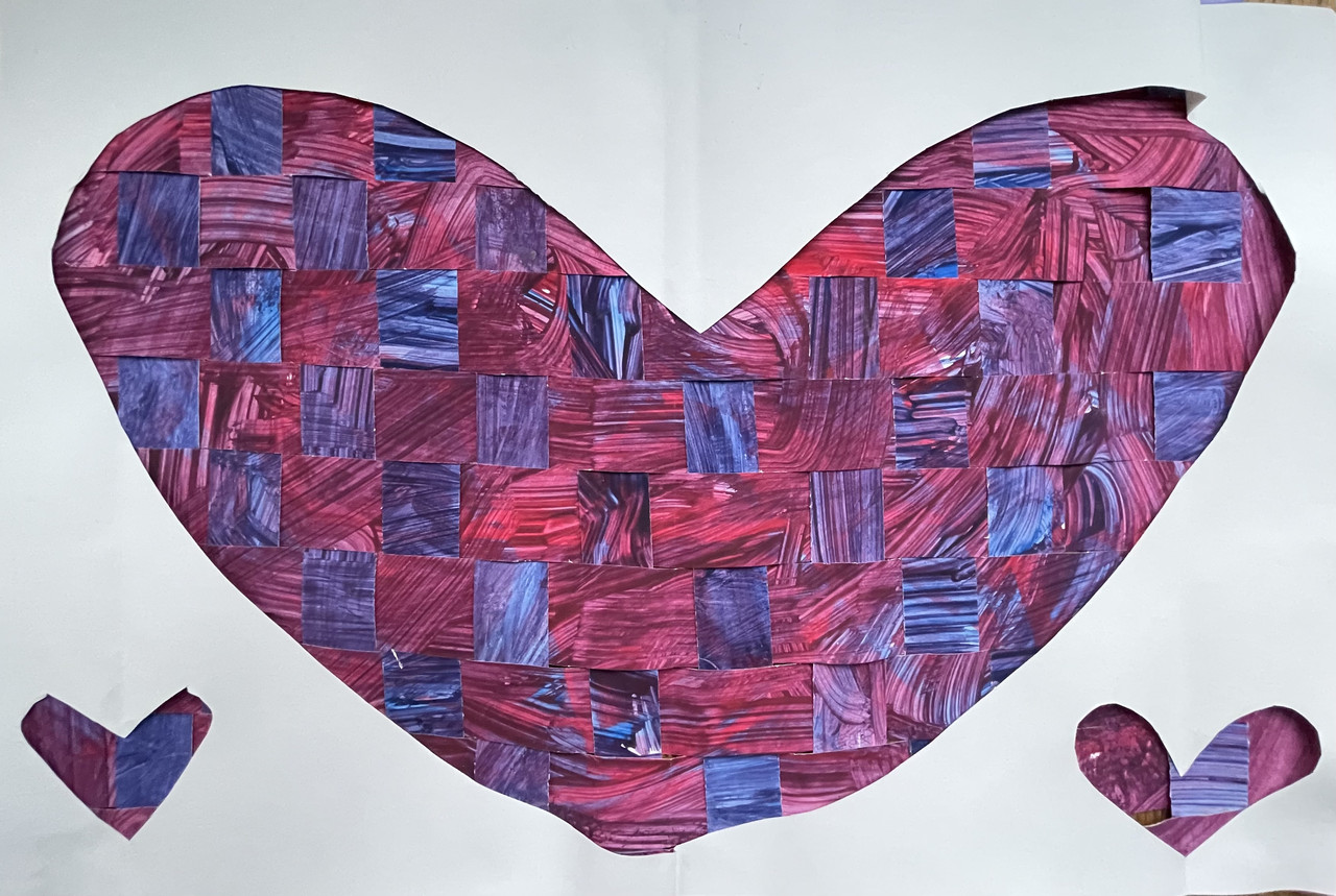A large heart is cut out of the center of a white piece of paper and two smaller hearts are cut out on the sides. Each heart appears to be made of woven pink and purple squares.