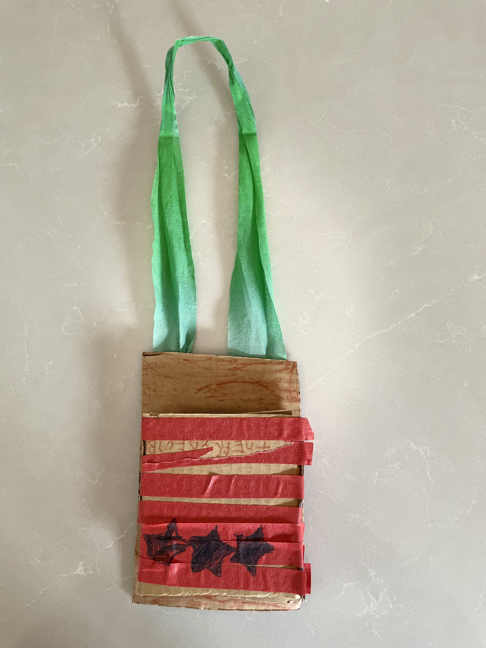 A rectangle of cardboard with a green "neck" string, carboard wrapped with red paper and 3 black stars.