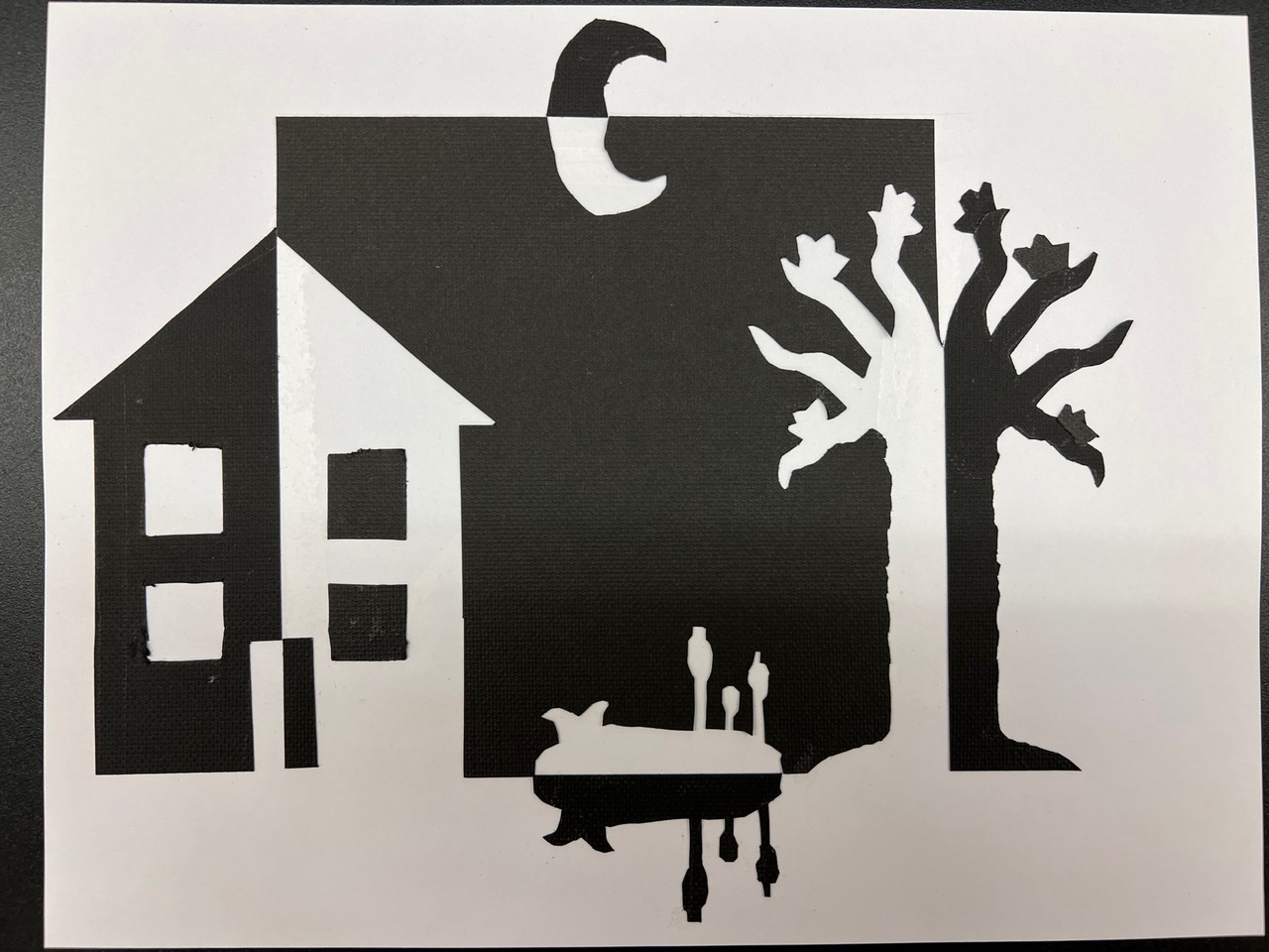 b/w paper cut into shapes of building, tree, and moon