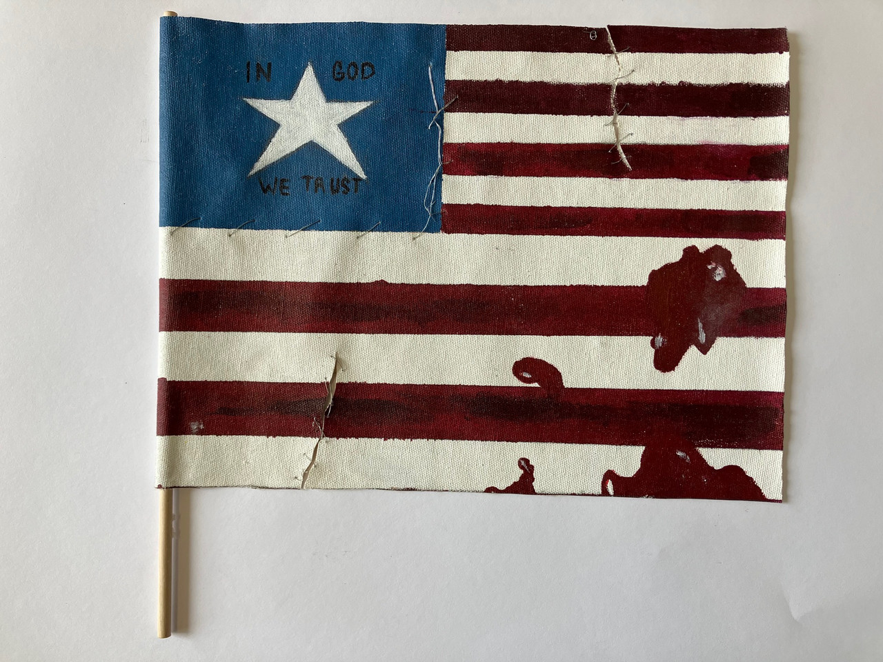 A mixed media artpiece of an American Flag with 1 star. There are written words around the star reading "In God We Trust."