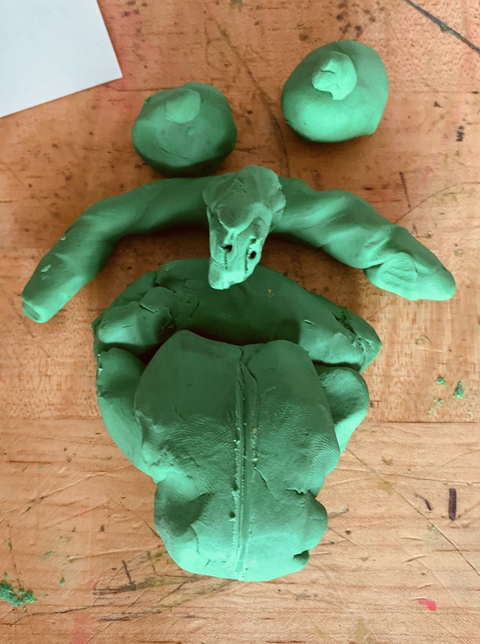 Green clay is molded to create two eyes, a nose, and a mouth with a tongue sticking out of it.