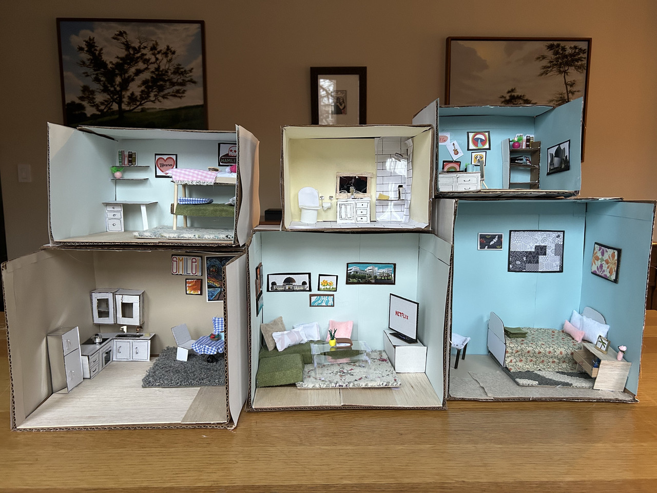 A collection of dioramas. Each one is a room of a miniature house: 2 bedrooms, 1 office, 1 kitchen, 1 living room, 1 bathroom.