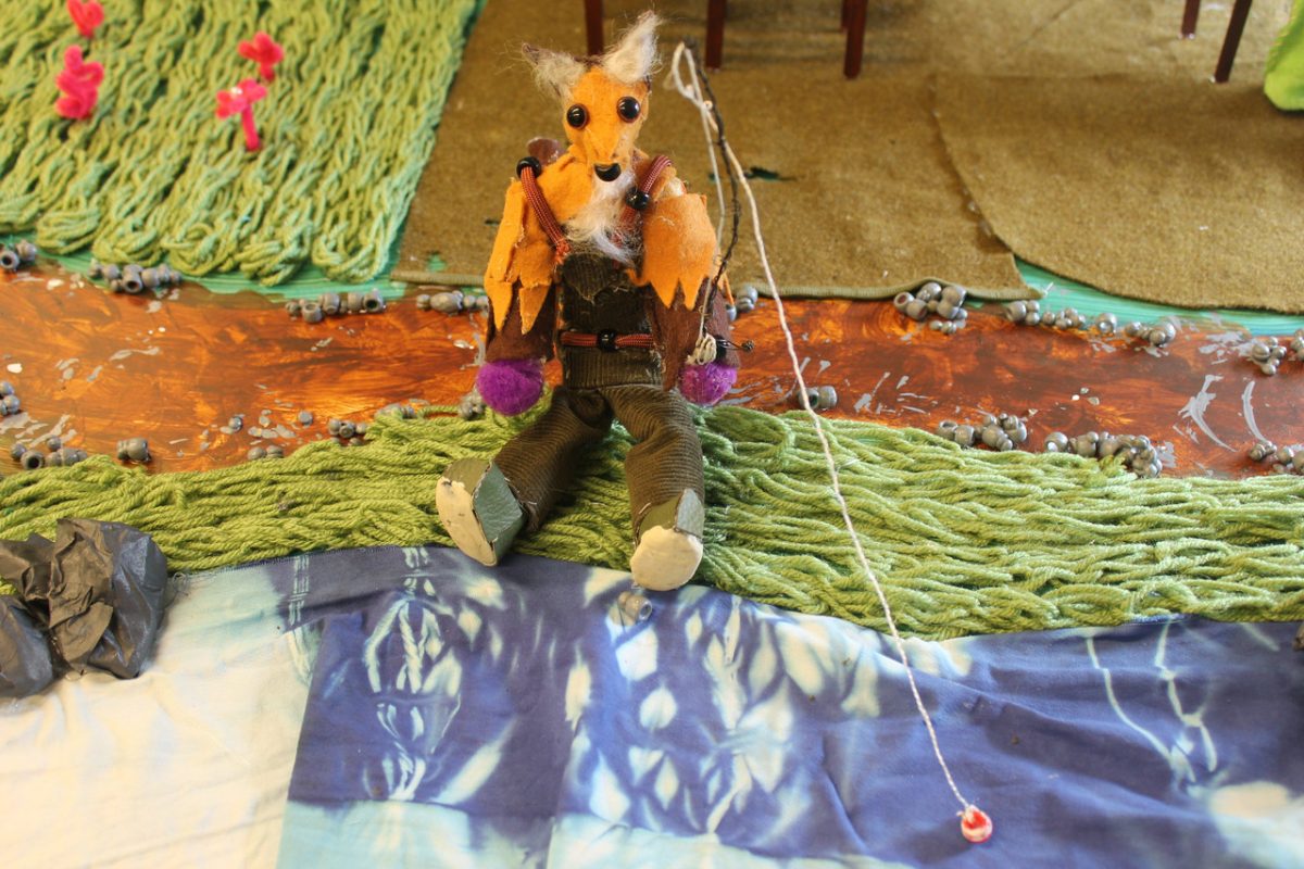 A fox puppet fishing on a river.
