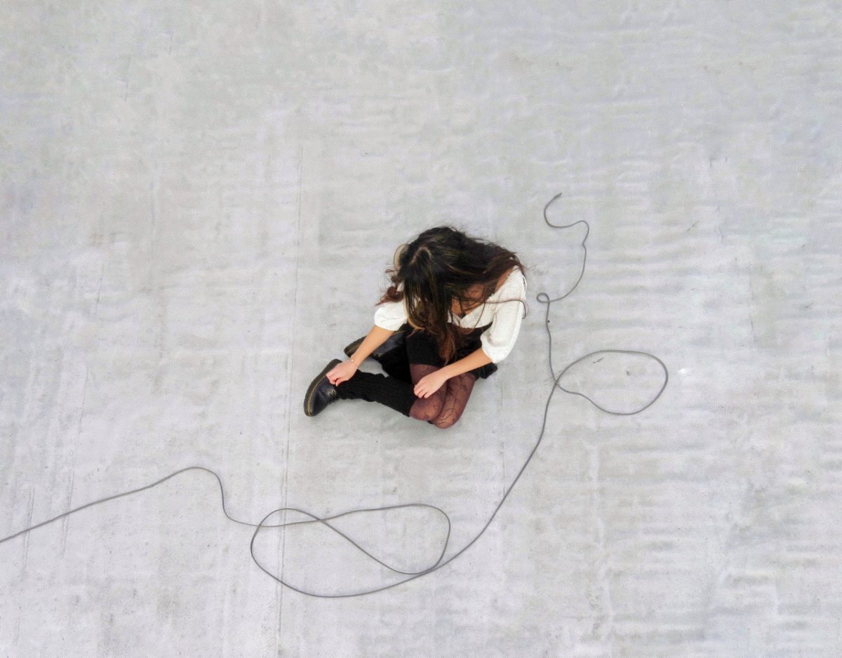 A photo of a person sitting on pavement with wire curved around the side of their body.