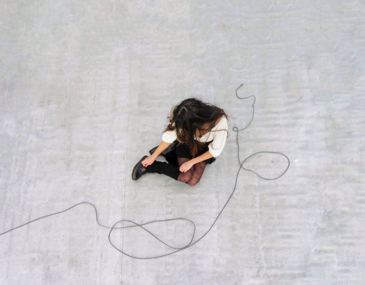 A photo of a person sitting on pavement with wire curved around the side of their body.