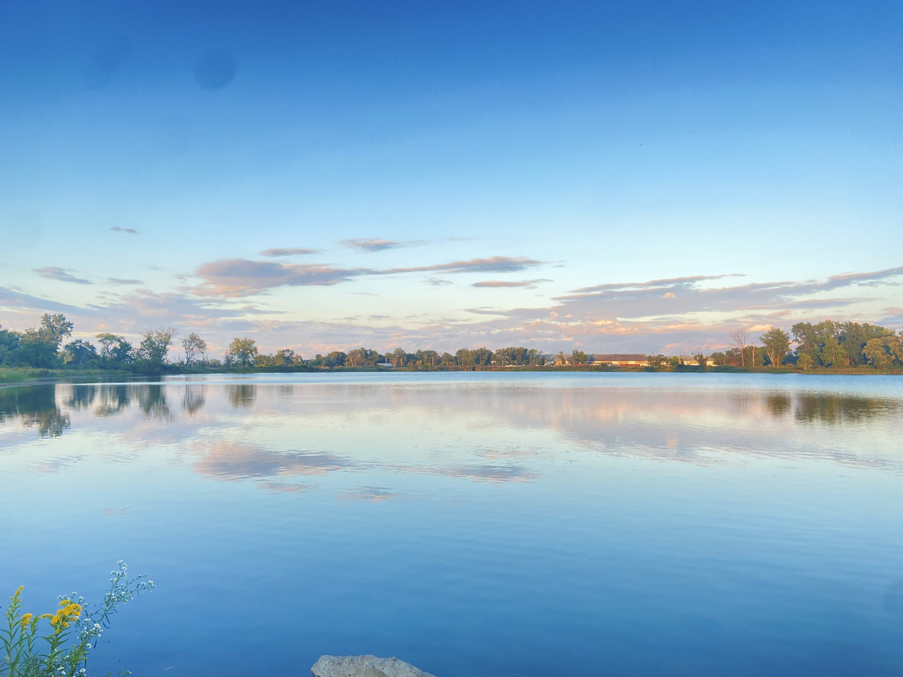 A photo of a lake with a blue sky and clouds reflecting on it.