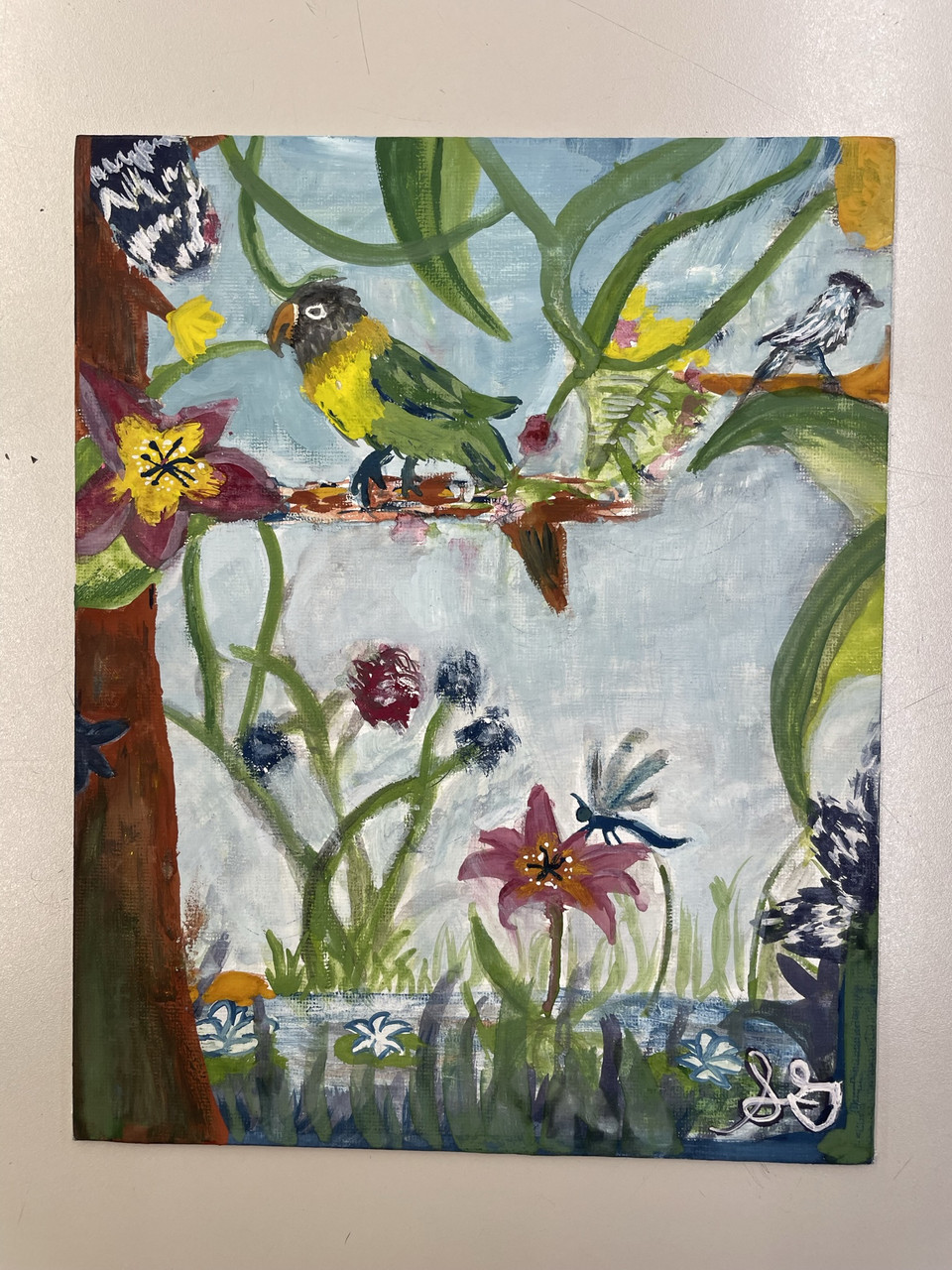 A green and yellow bird sits on a brown tree branch. It is surrounded by vines and flowers near it and on the ground below it.