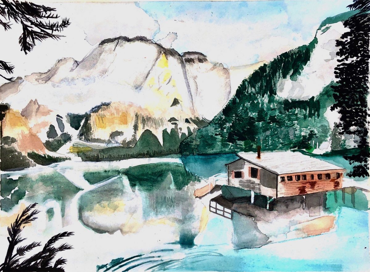 A cabin on a lake with mountains behind.