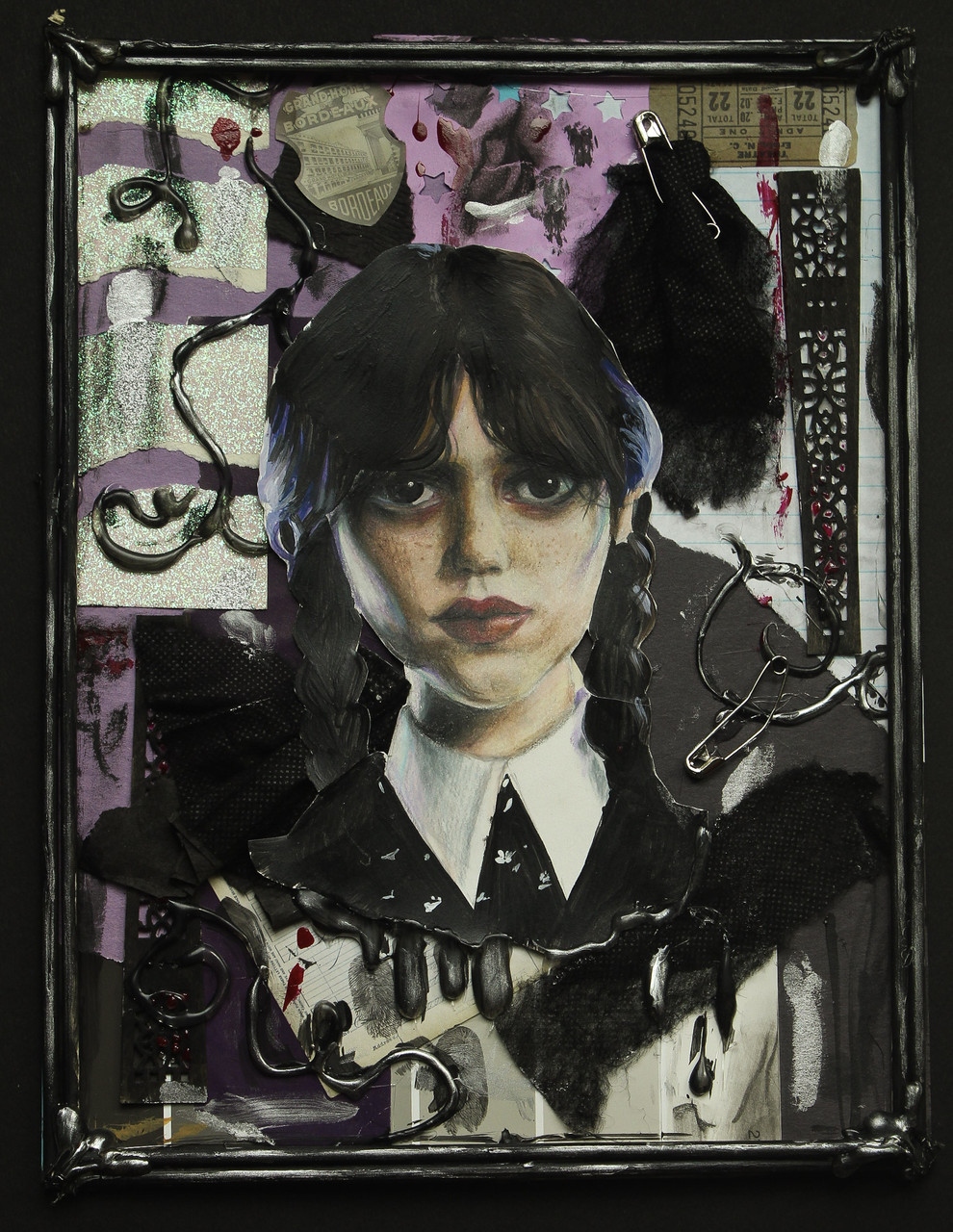 A collage of Wednesday Adams at the center. The background has various paper cutouts in silver, black and purple. There are 2 safety pins. One is adhering a piece of black cloth.