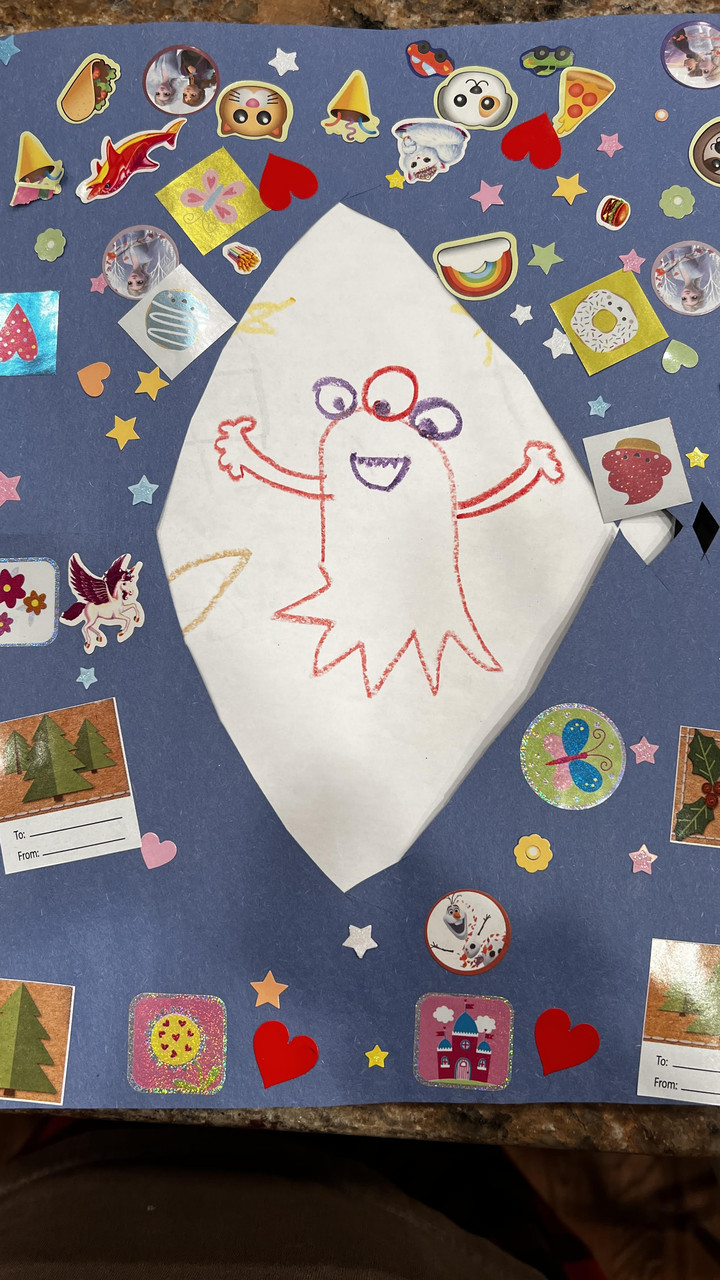 Crayon drawing of a character named beaker on white paper. The white paper is surrounded by blue paper which is covered in stickers.