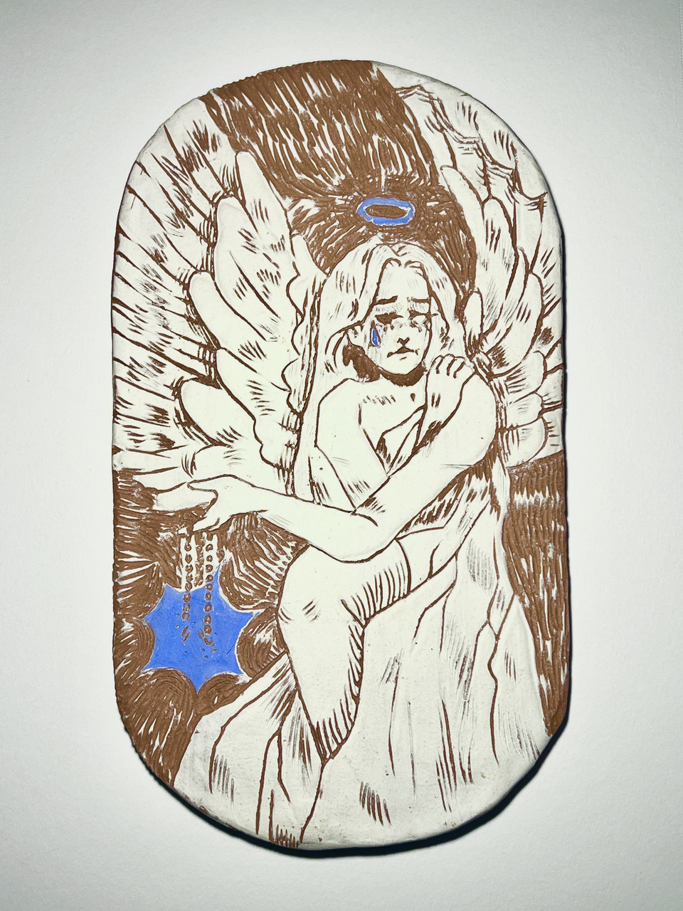 A rounded oval clay piece with a white angel.