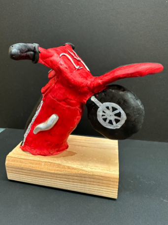 Sculpture of a red motorcycle lofted up on a wood block.