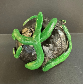 Ceramic black ball covered in a green snake that is tangled around it.