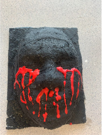 A dark face created from plaster with red dripping from the eyes and nose to represent blood.