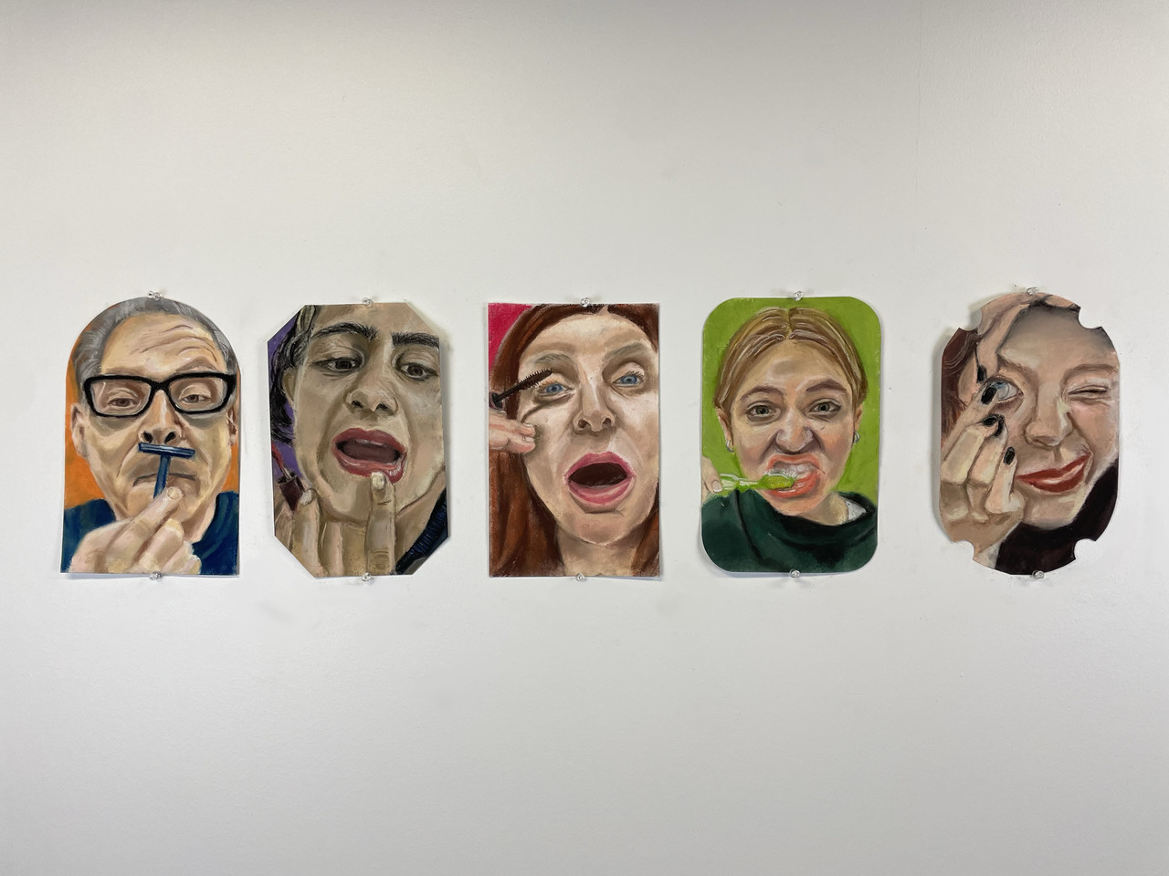 Paintings on various cut canvases that depict peoples' faces alike to ones they make in mirrors.