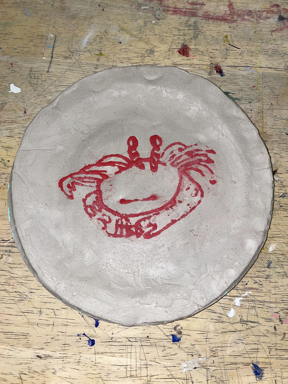 A clay piece with a red crab outline on it.