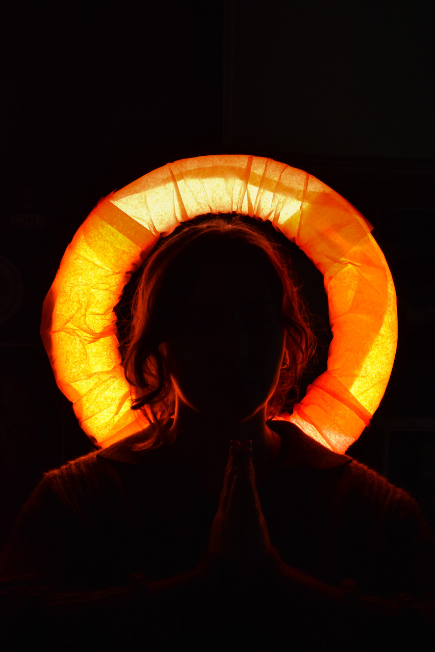 Photograph of a dark figure in front of a yellow glowing halo surrounding their head.