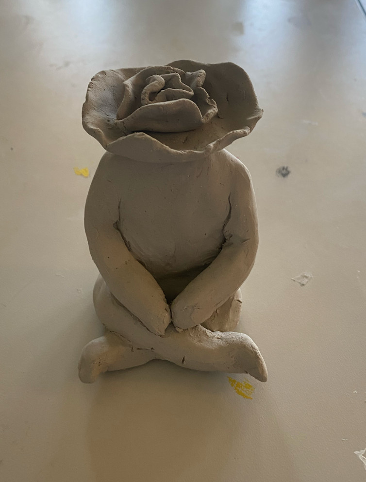 A sculptural piece of a person with a flower head sitting cross-legged.