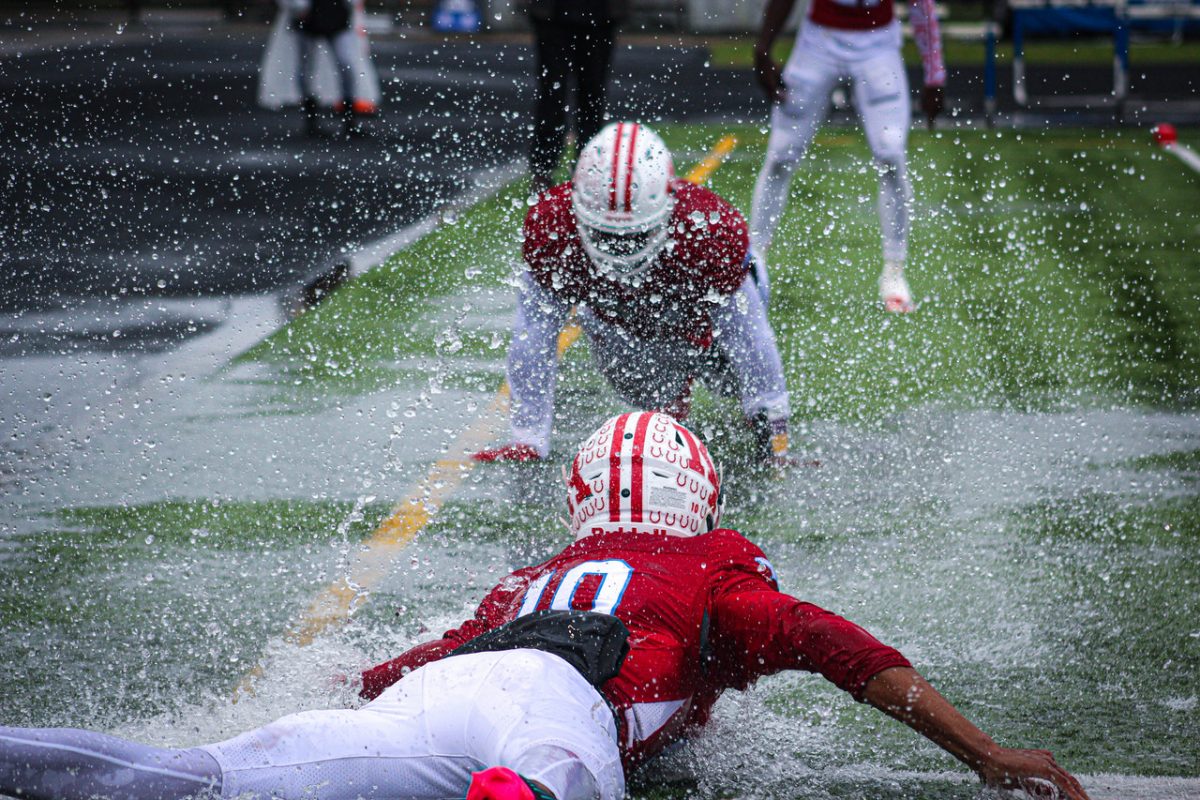 Photo of two football players in red sliding toward each other on wet field. Lots of water comes out of the field.