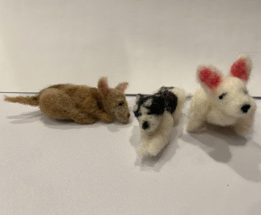 Three dogs left is brown and laying down middle is laying down and has a splotchy black and white coat right is sitting up and has completely white fur