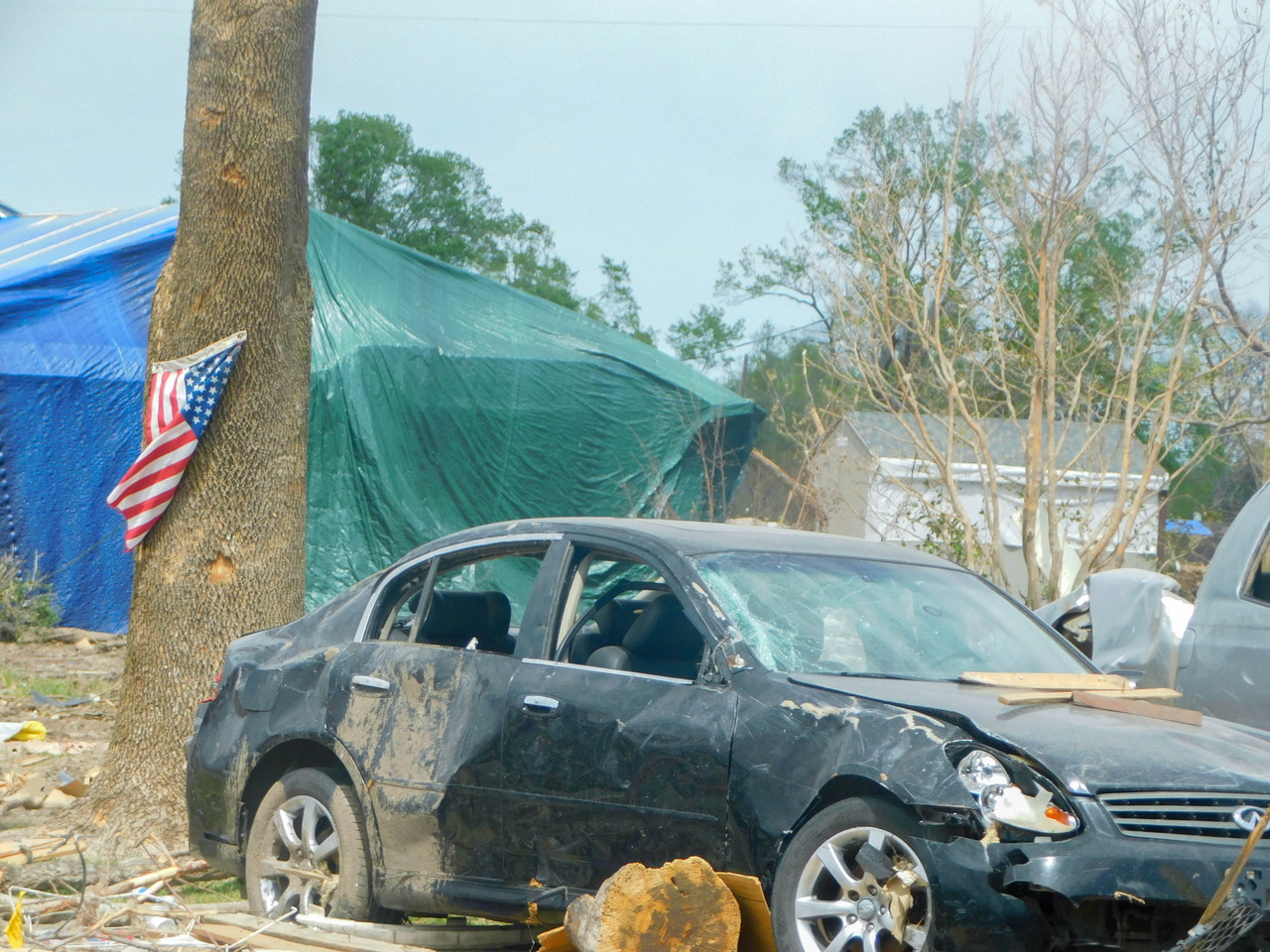 Photograph of a rundown car surrounded by a tent, trees, and an American flag