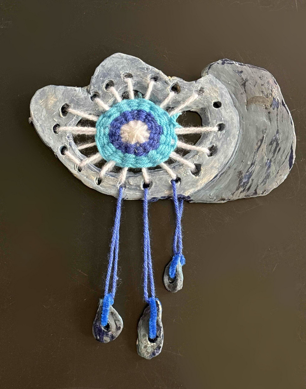 A sculpture piece made with yarn in a ceramic loom piece shaped like a cloud, with raindrops hanging from it.