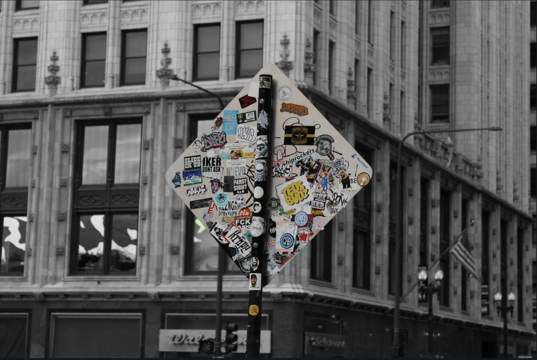 Back of yield sign with stickers highlighted in color against black and white building.