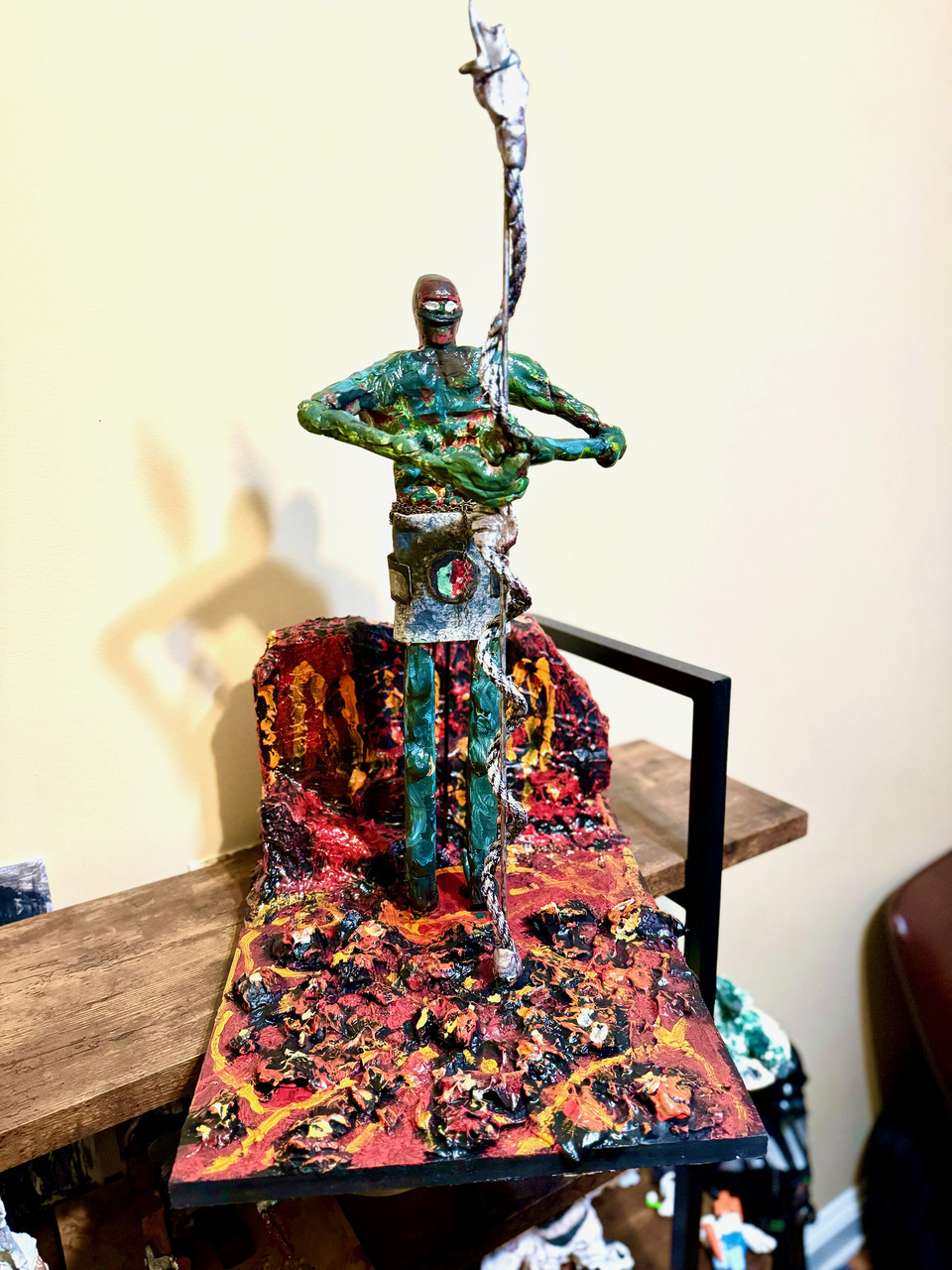 A 3D sculpture of a large human-like figure standing on a platform. Everything is covered in mixed colors