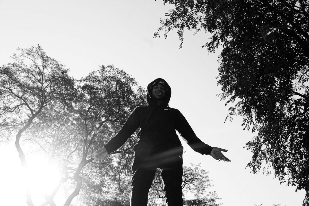 Black and white photo of male figure taken from below. Trees glow behind him.
