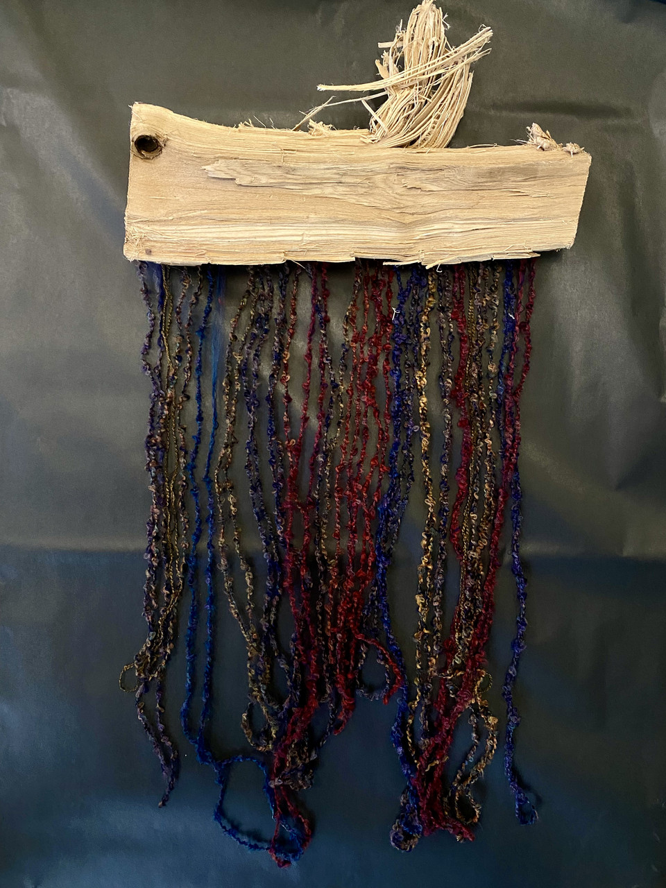 Mixed media work of muted colors made of wood and string hanging down.