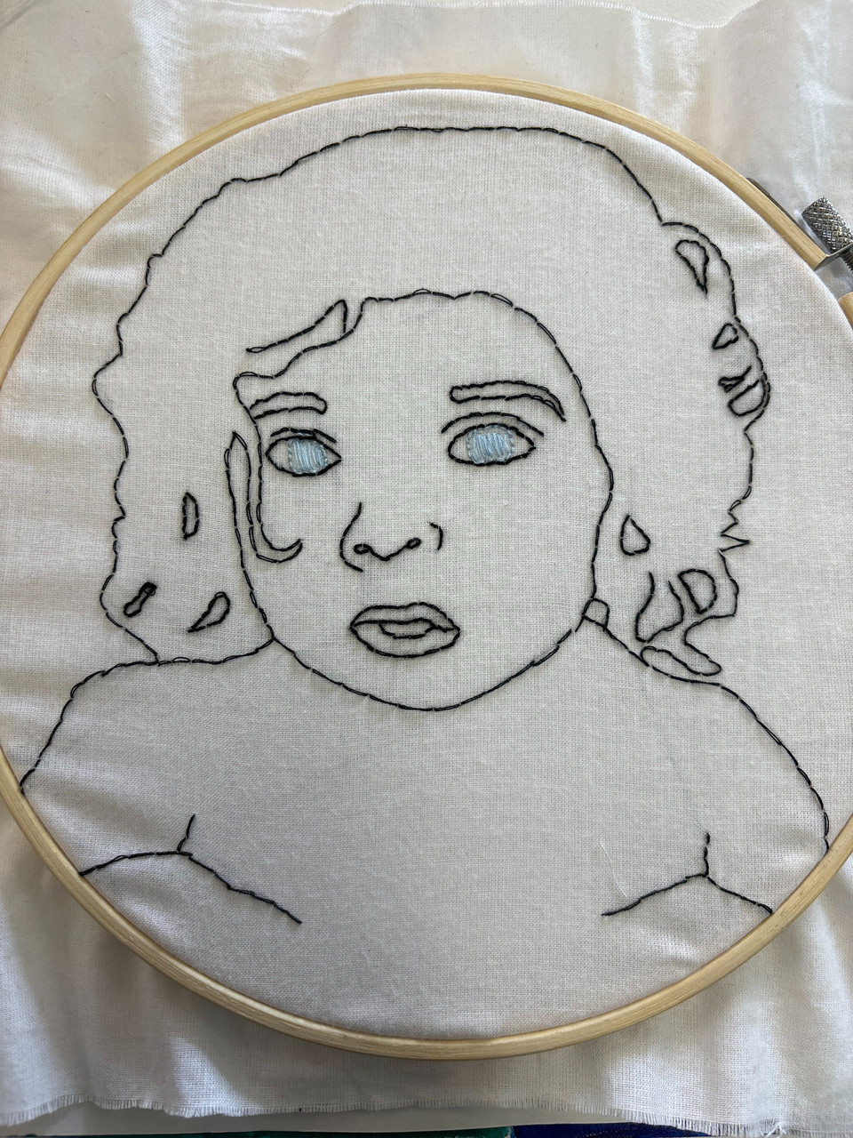 Embroidered black thread on white fabric of face and shoulders. Figure has embroidered blue eyes.