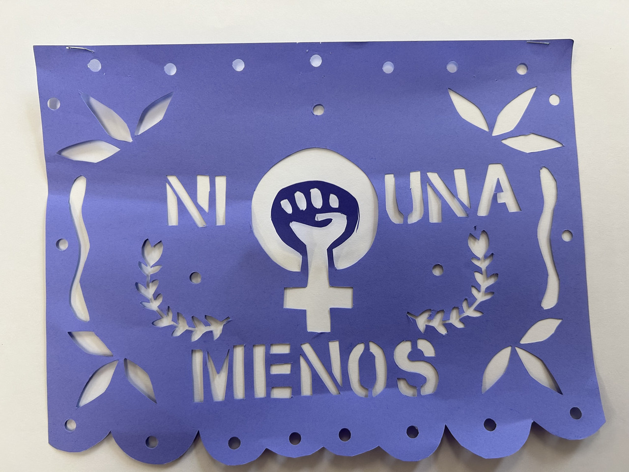 A cut paper with the words "Ni Una Menos" with a fist inside the female sign in the middle.