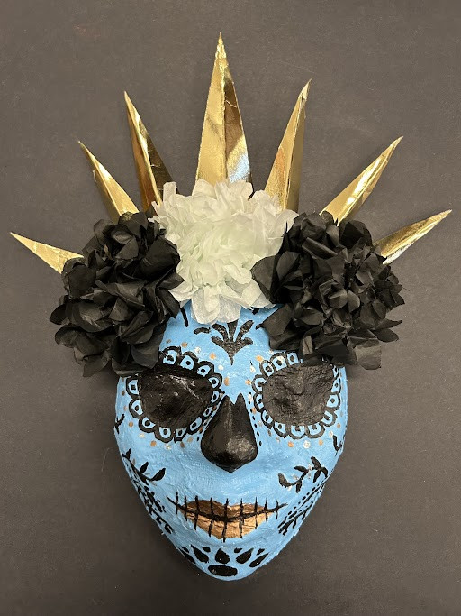 A blue mask of a catrina figure with gold spikes coming out the head.