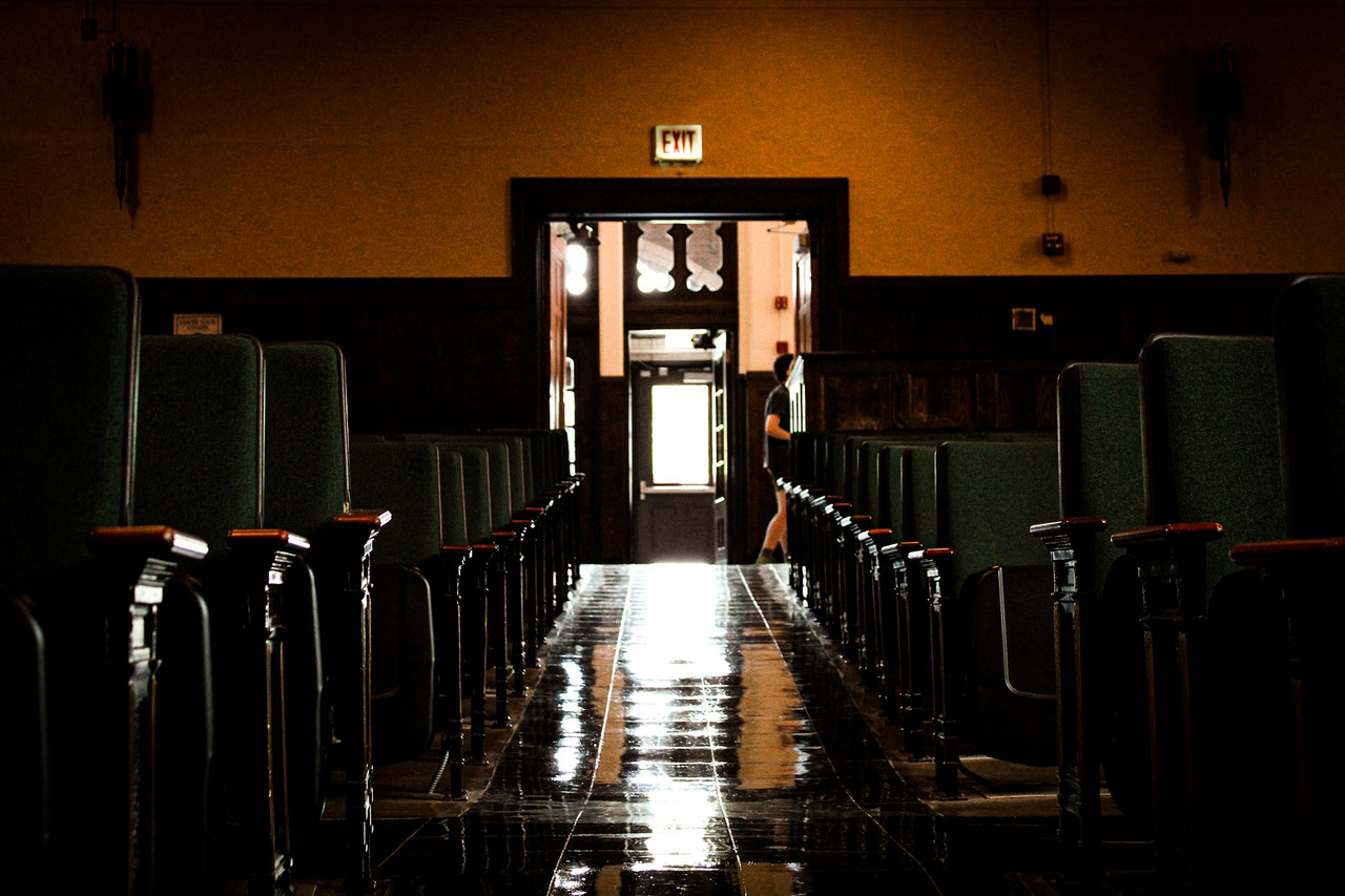 An empty hallway of a theater leads to a door with sun beaming in